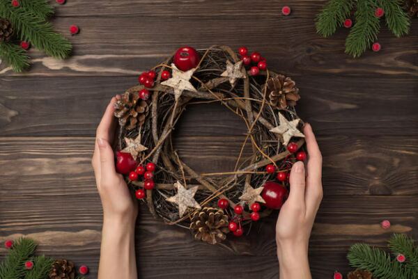 foto de primeira pessoa de galhos de pinheiro e maos femininas segurando uma guirlanda de galho de natal com bagas de azevinho e pinhas no fundo da mesa de madeira escura isol - Booking-Senior.com